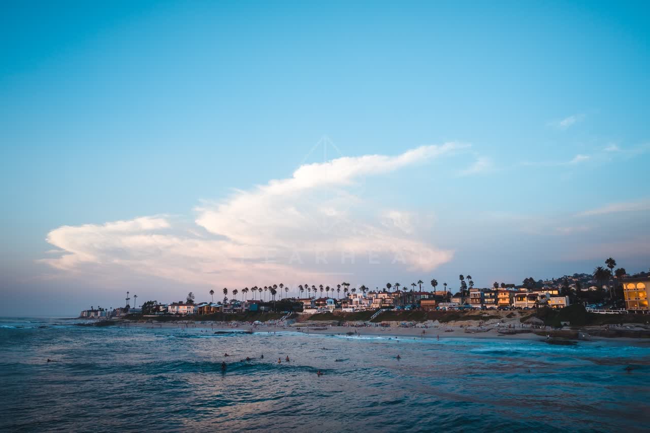 Low aerial view of the beach, the surf and palm trees at Windansea, with swimmers in the water.