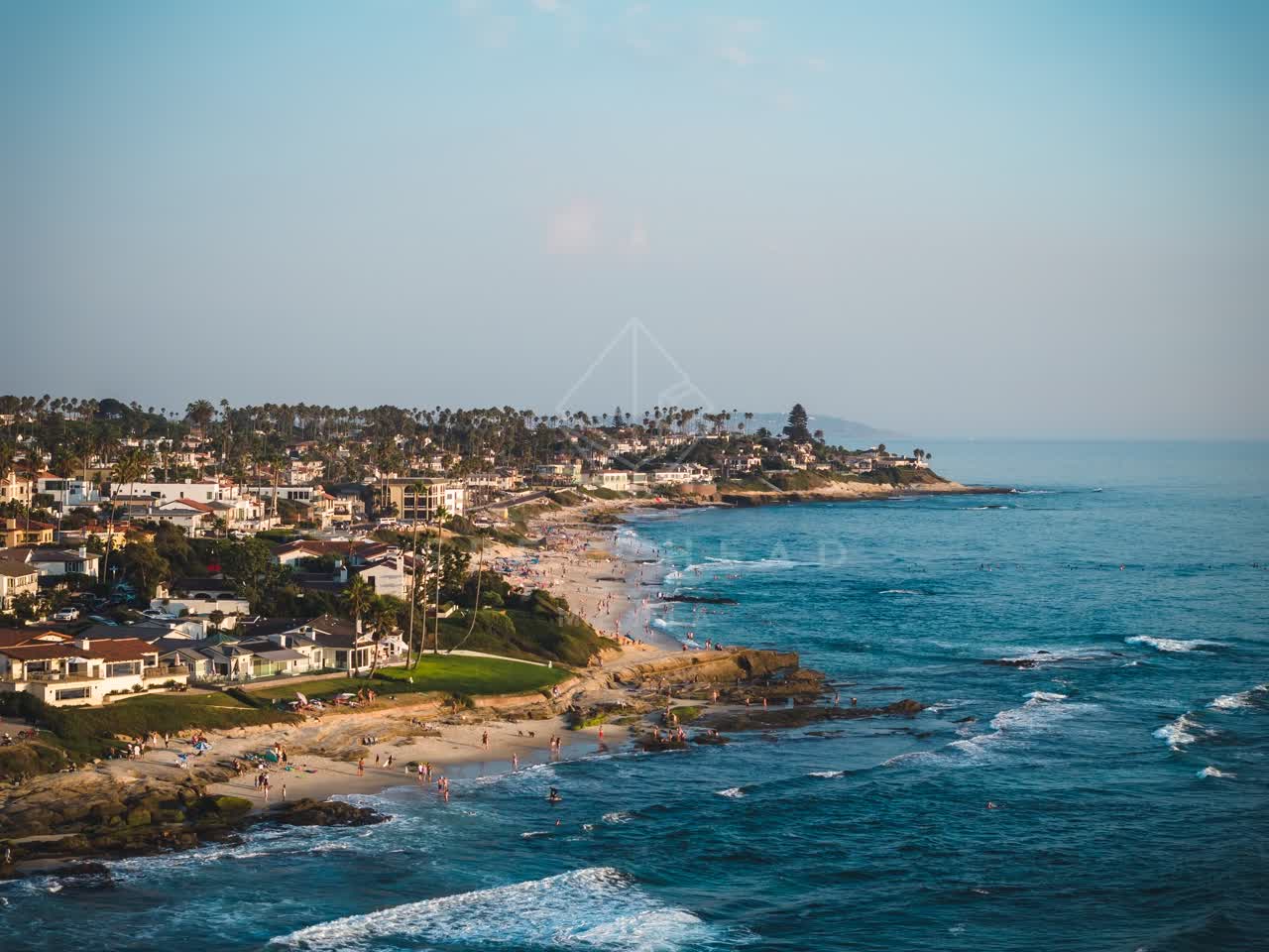 Aerial view of the beach, the surf and palm trees at Windansea, with people walking.