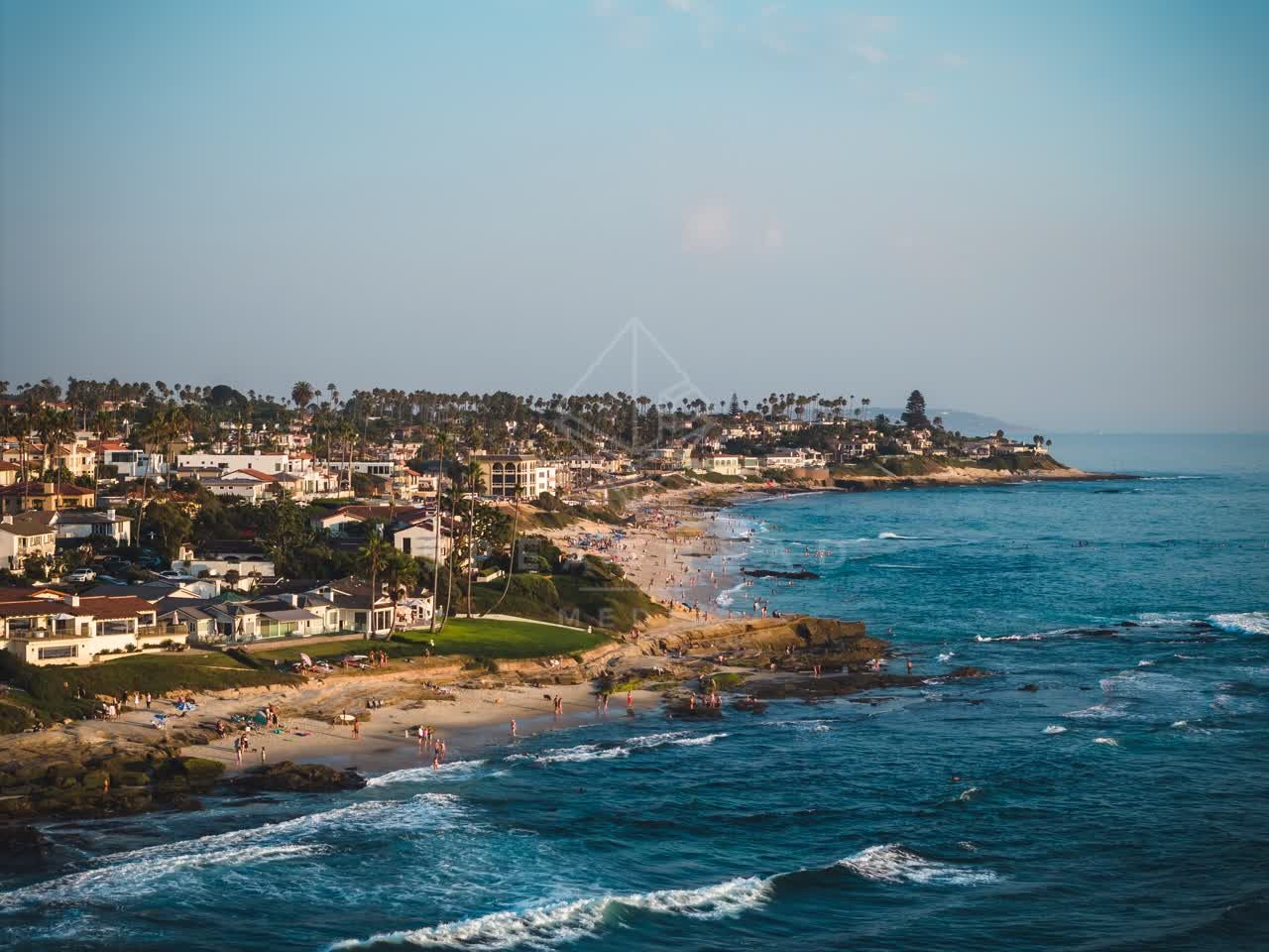 Aerial view of the beach, the surf and palm trees at Windansea, with people walking.