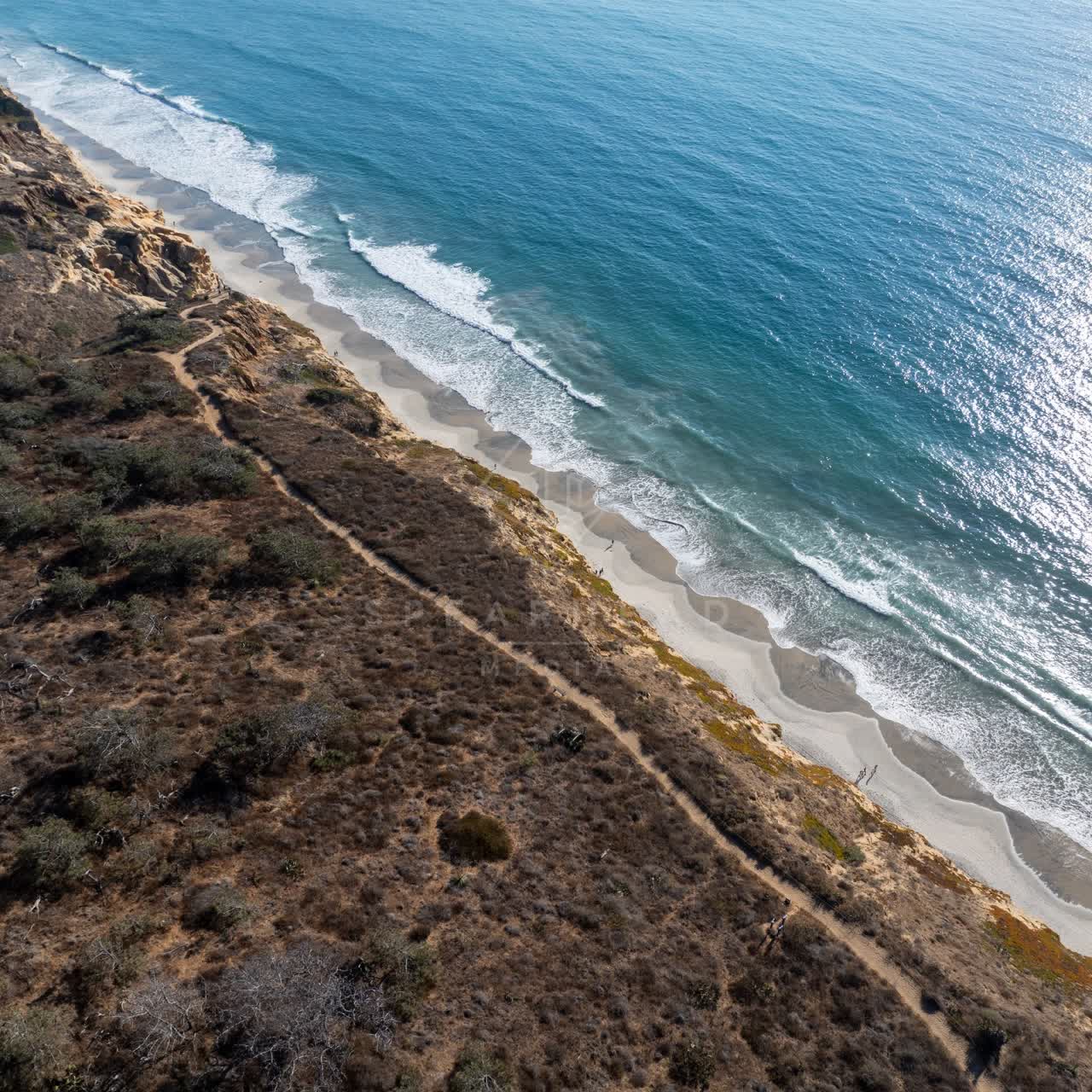 Aerial view of the cliffs, the surf and the ocean at Torrey Pines, with people walking.