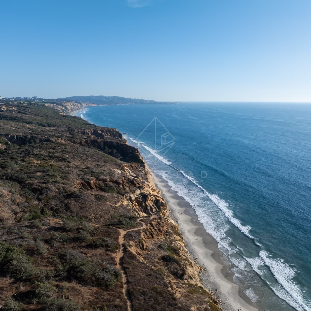 Aerial view of the cliffs, the surf and the ocean at Torrey Pines, with people walking.