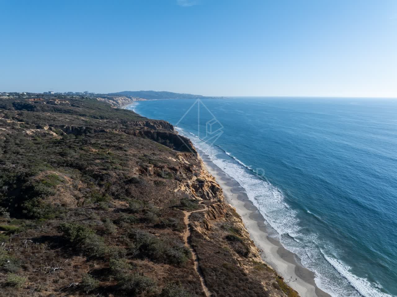 Aerial view of the cliffs, the surf and the ocean at Torrey Pines, with people walking.