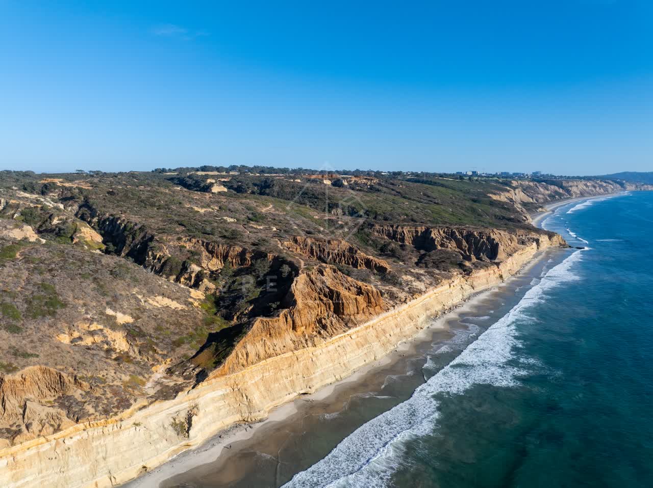 Aerial view of the cliffs, the surf and the ocean at Torrey Pines, with people walking.