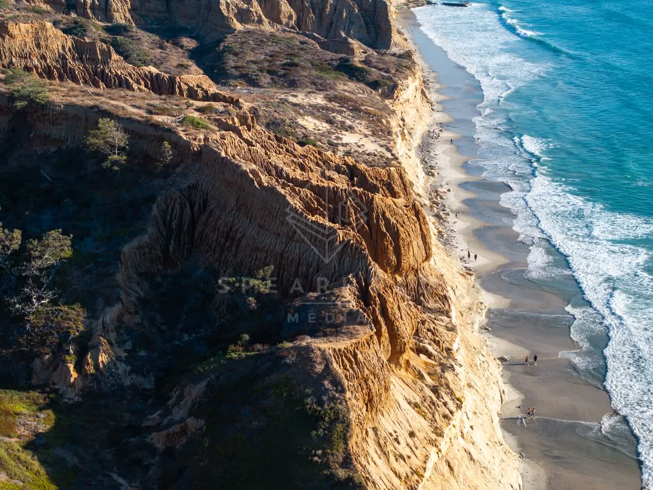 Aerial view of the cliffs, the surf and the ocean at Torrey Pines, with people walking.