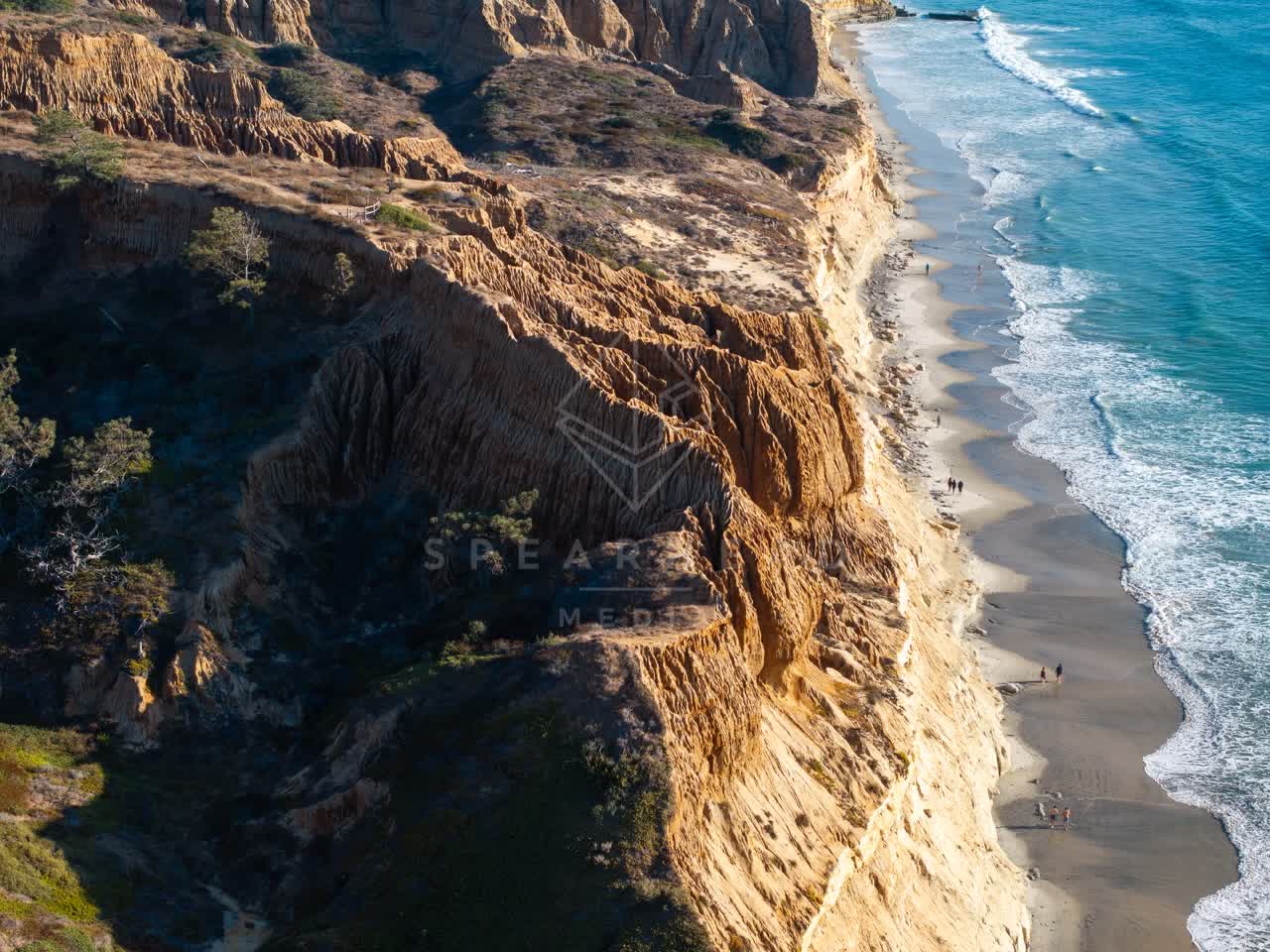 Aerial view of the cliffs, the surf and the ocean at Torrey Pines, with people walking.