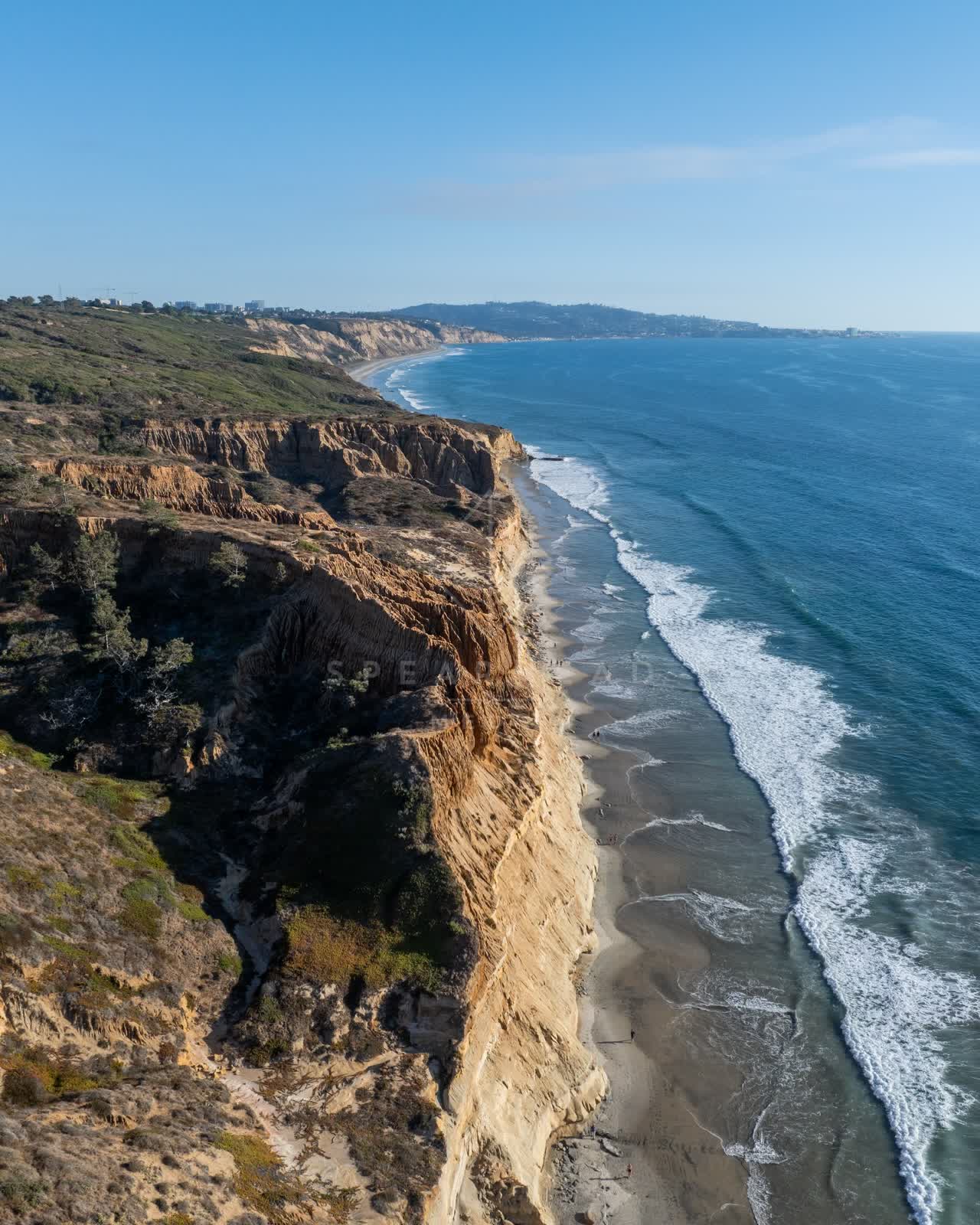 Aerial view of the cliffs, the surf and the ocean at Torrey Pines, with people walking.
