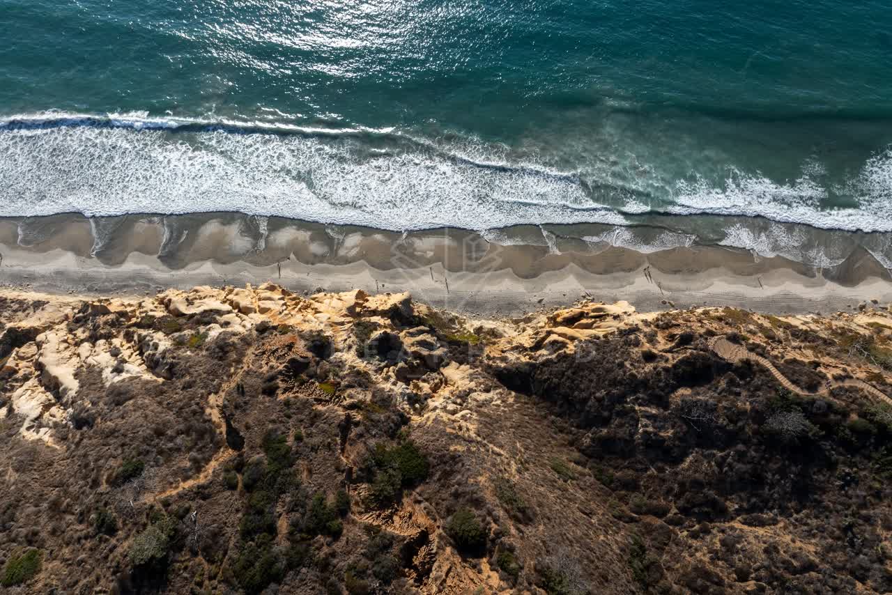 Aerial view of the cliffs, the surf and the ocean at Torrey Pines, with people walking.