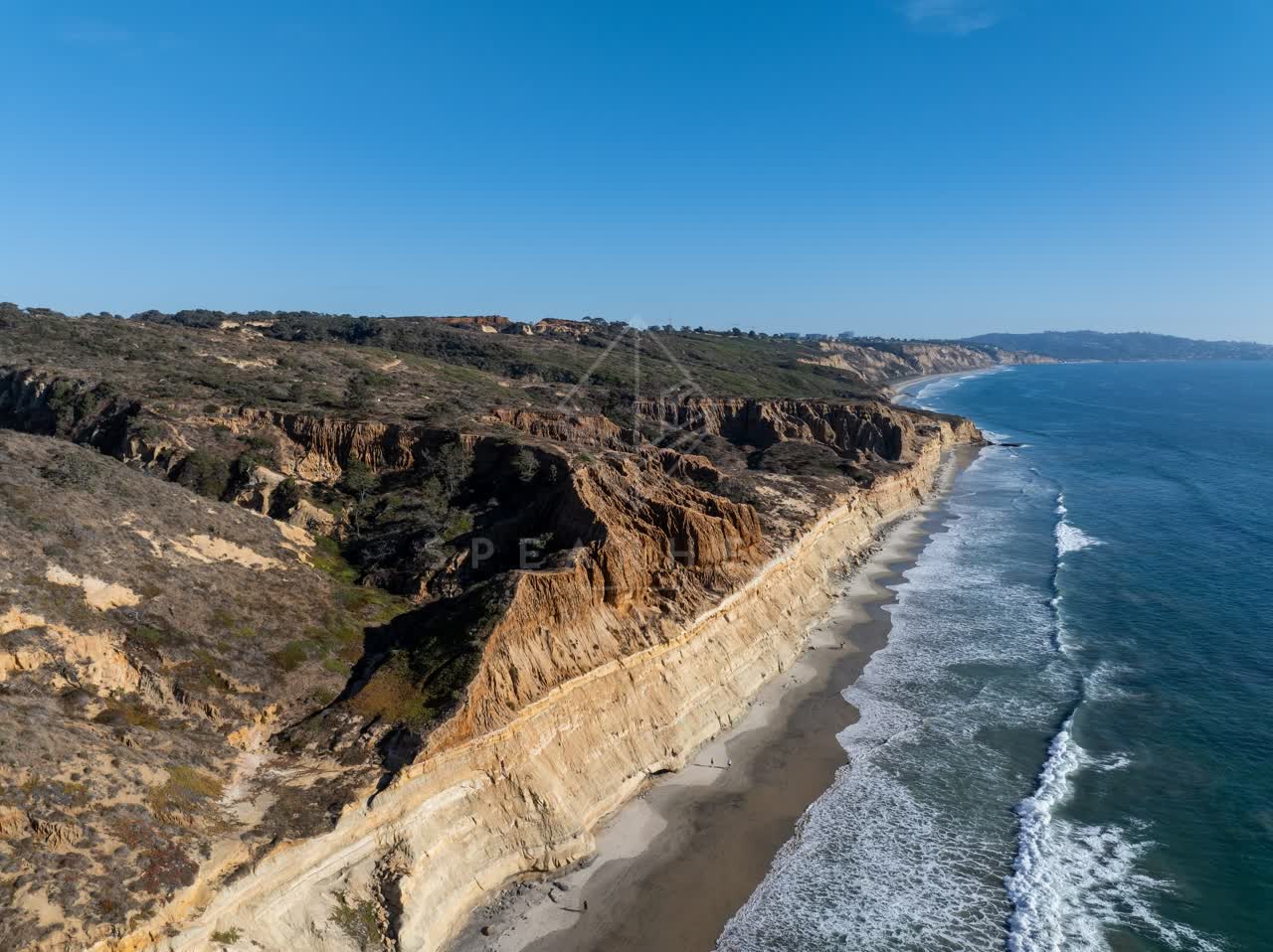 Aerial view of the cliffs, the surf and the ocean at Torrey Pines, with people walking.