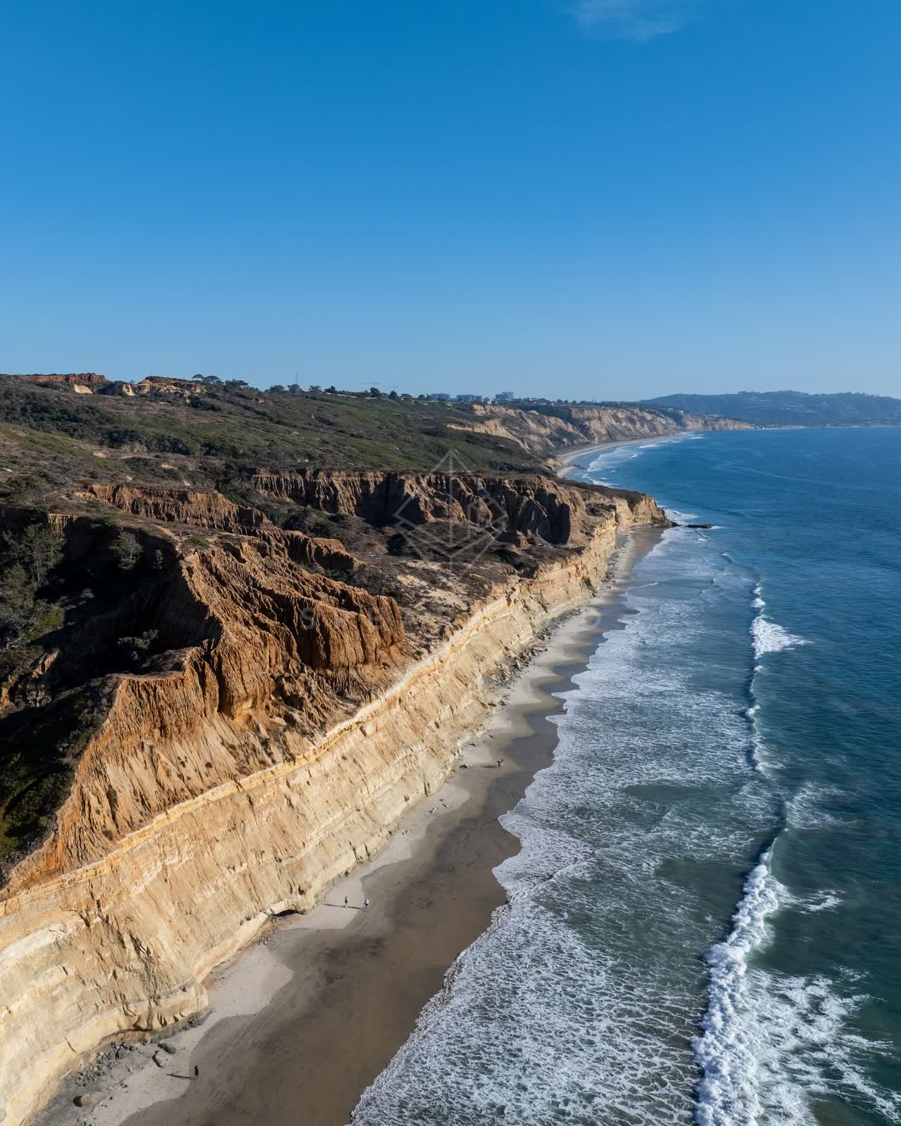 Aerial view of the cliffs, the surf and the ocean at Torrey Pines, with people walking.