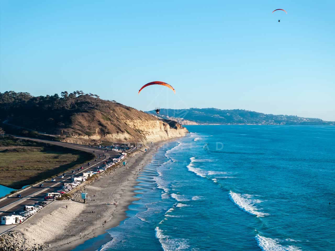 Aerial view of the cliffs, the surf and the ocean at Torrey Pines, with a crowd gathered.