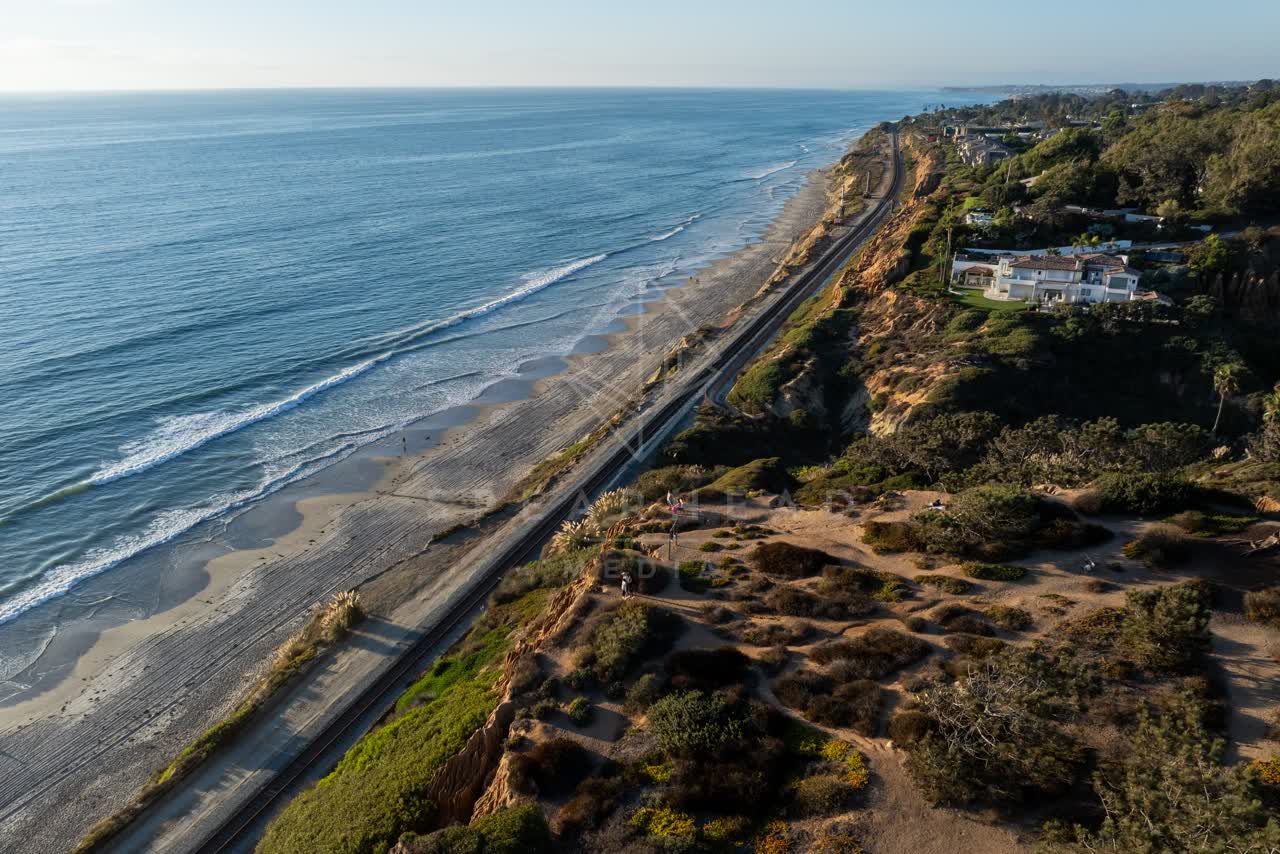 Aerial view of the cliffs, the surf and palm trees in Del Mar, with people walking.