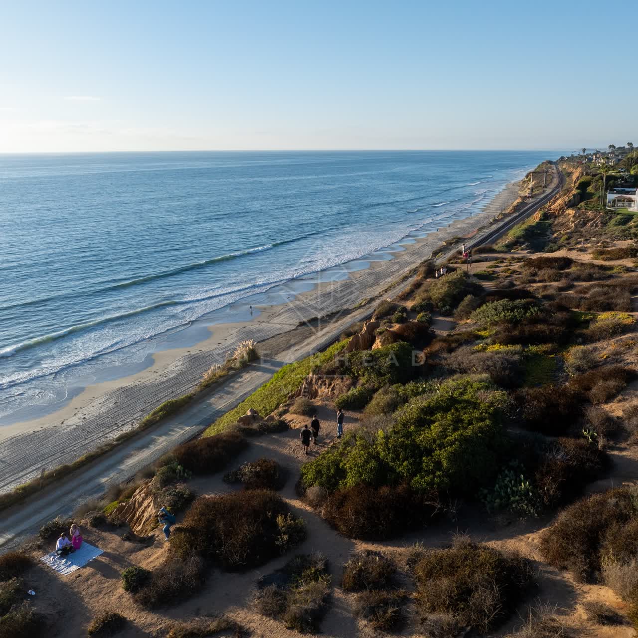Aerial view of the cliffs, the ocean and homes in Del Mar, with people walking.