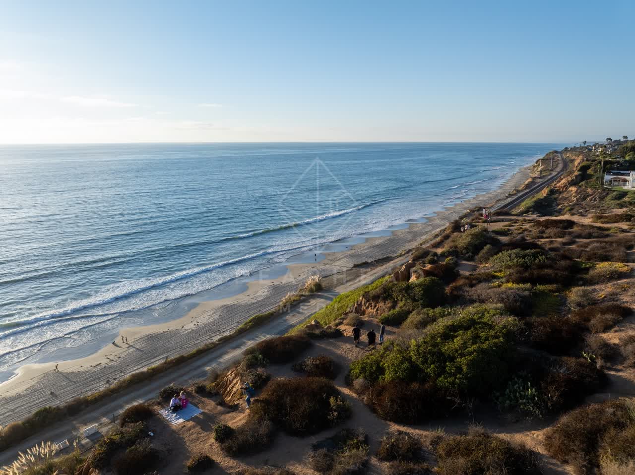 Aerial view of the cliffs, the surf and the ocean in Del Mar, with people walking.