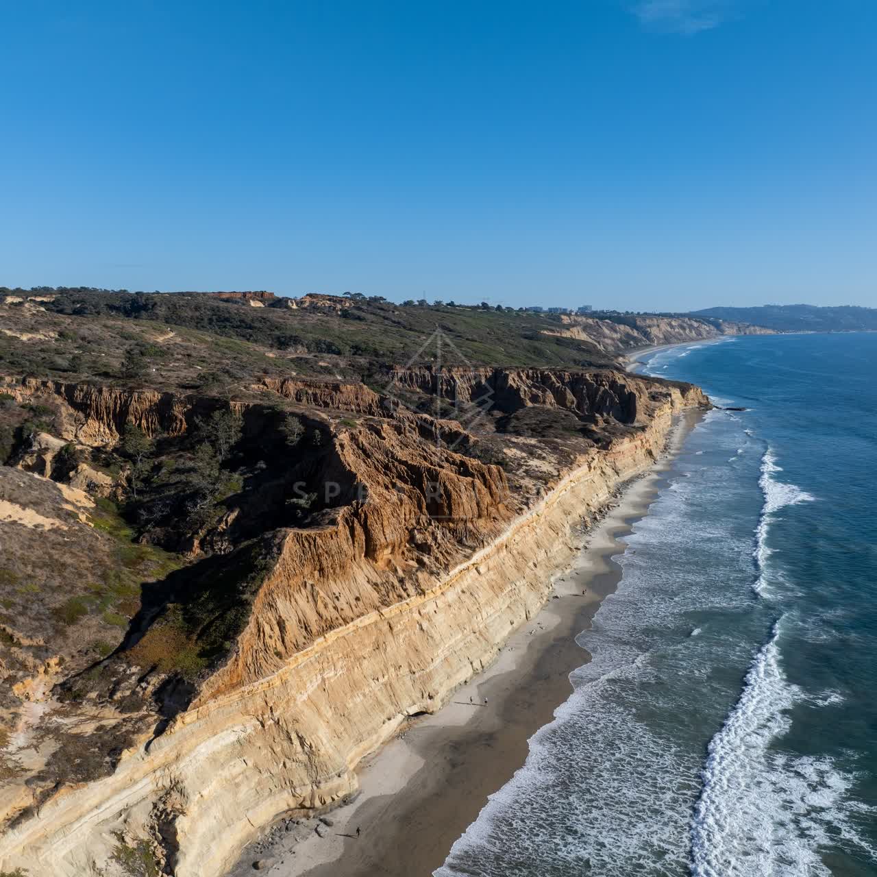 Aerial view of the cliffs, the surf and the ocean at Torrey Pines, with people walking.