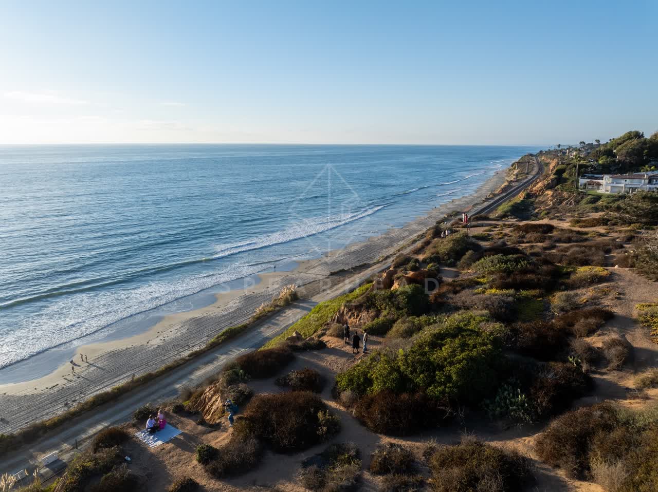Aerial view of the cliffs, the ocean and homes in Del Mar, with people walking.
