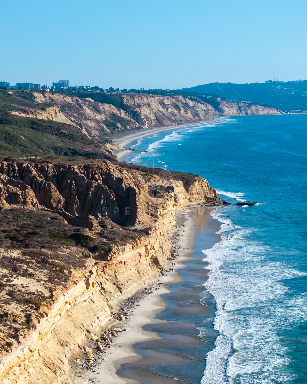 Aerial view of the cliffs, the surf and the ocean at Torrey Pines, with people walking.