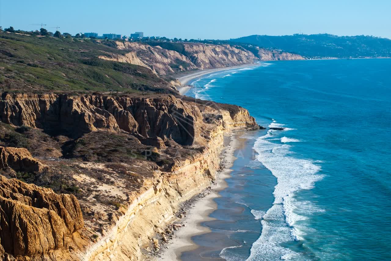 Aerial view of the cliffs, the surf and the ocean at Torrey Pines, with people walking.