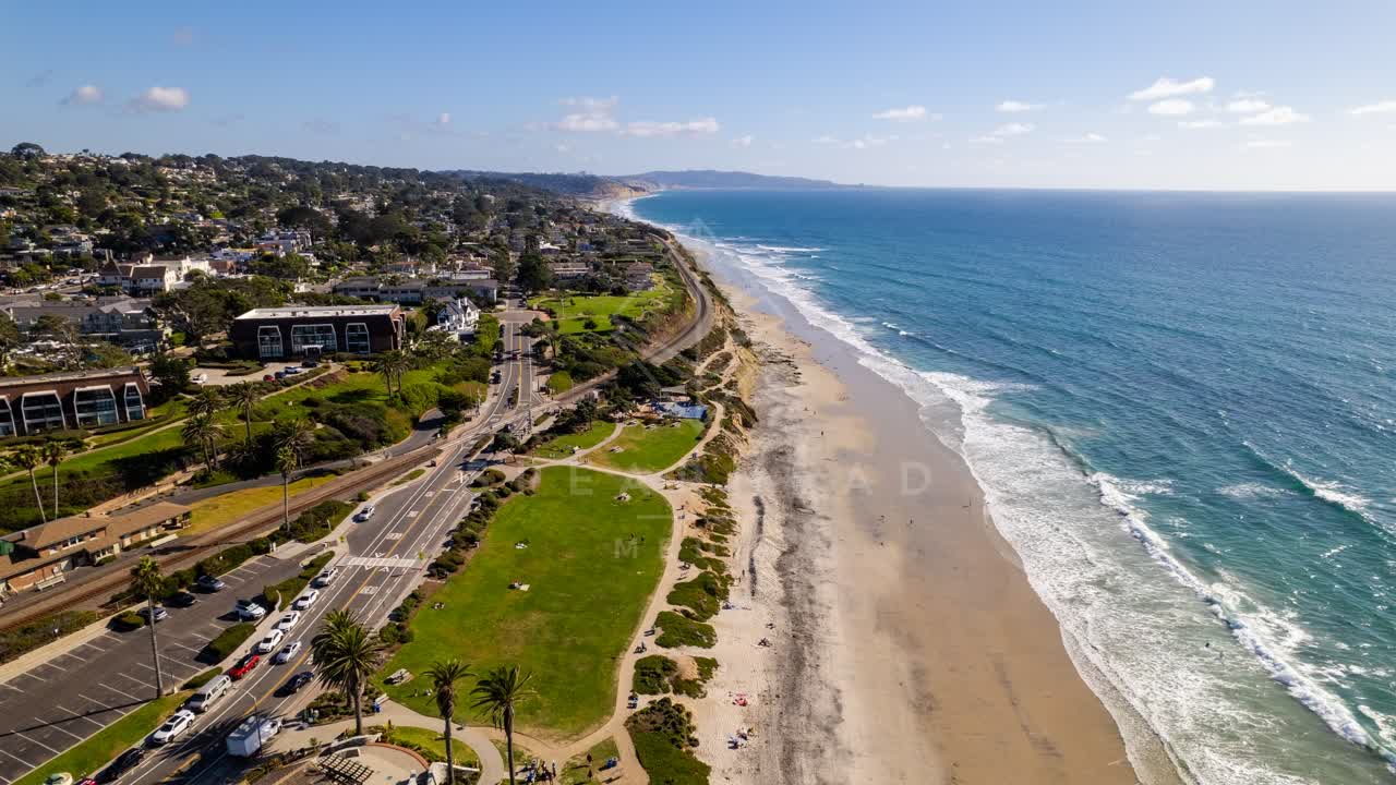 Aerial view of the beach, the surf and palm trees at Powerhouse Park, with people walking.