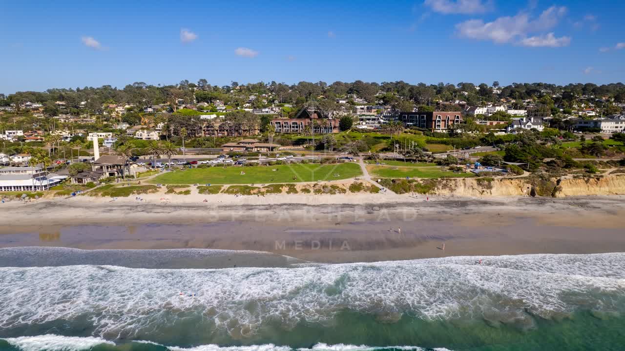 Aerial view of the beach, the surf and palm trees at Powerhouse Park, with people walking.