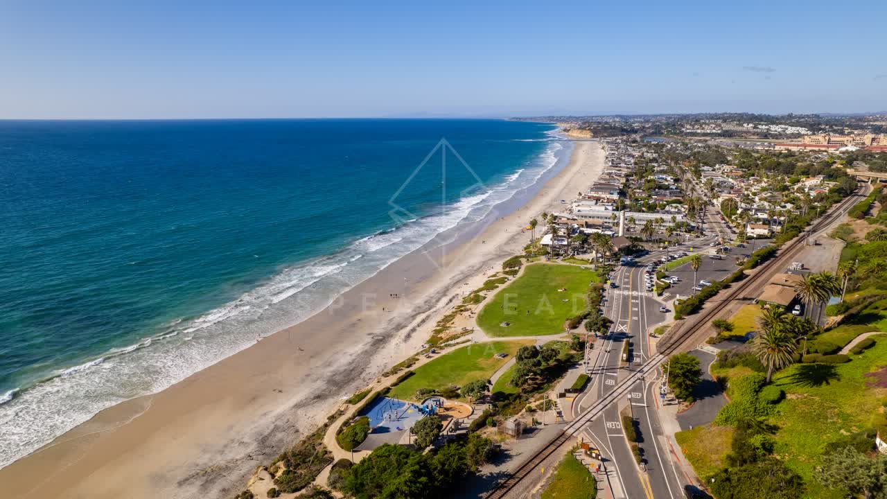 Aerial view of the beach, the surf and palm trees at Powerhouse Park, with people walking.