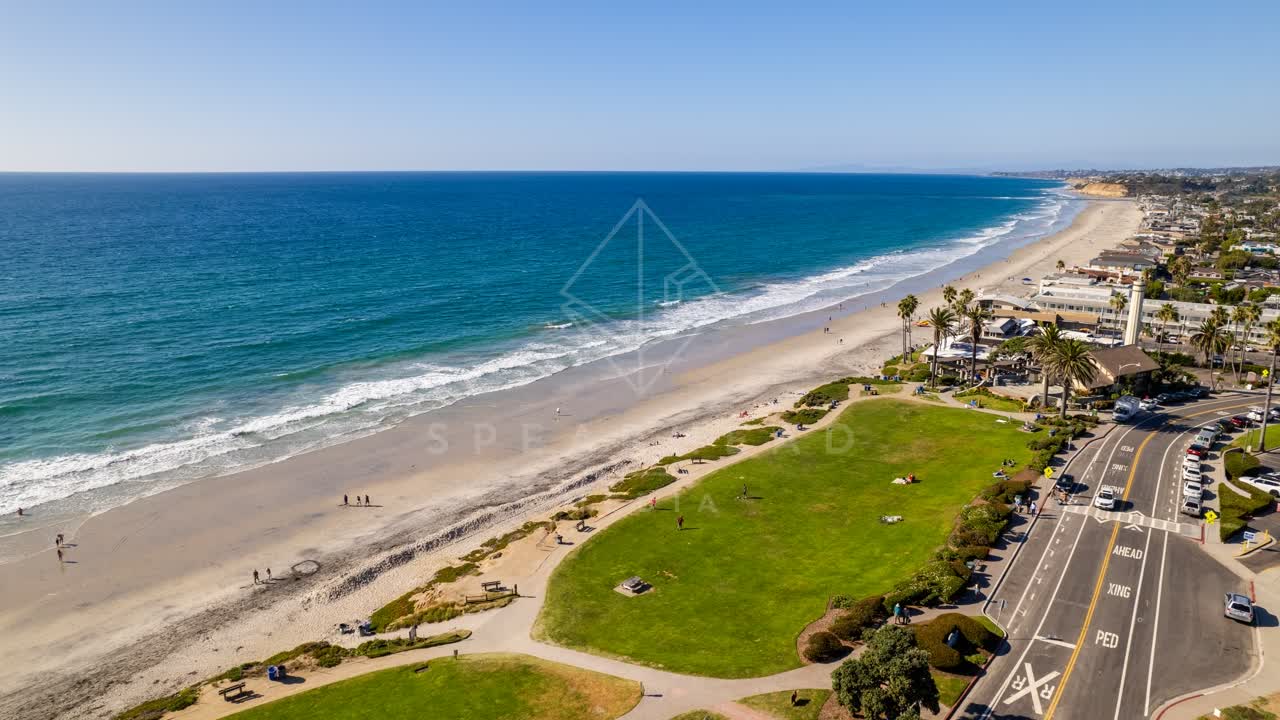 Aerial view of the beach, the surf and palm trees at Powerhouse Park, with people walking.