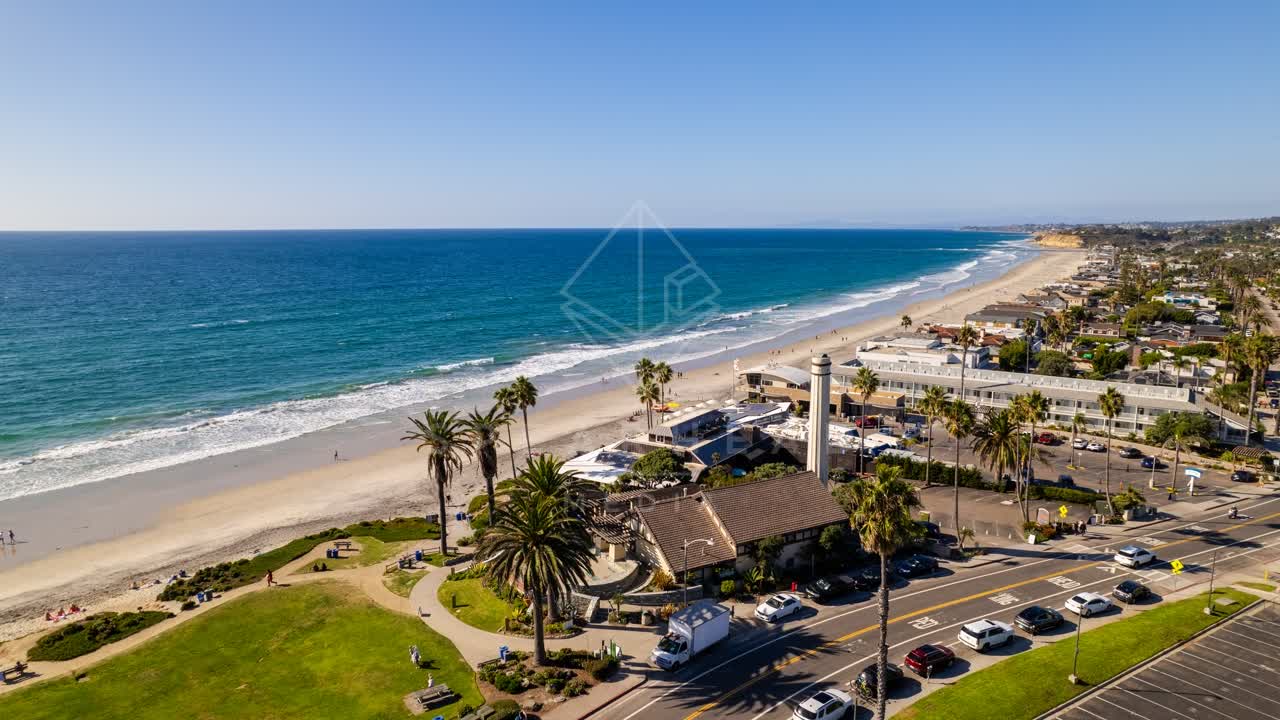 Aerial view of the beach, palm trees and the ocean at Powerhouse Park, with people walking.