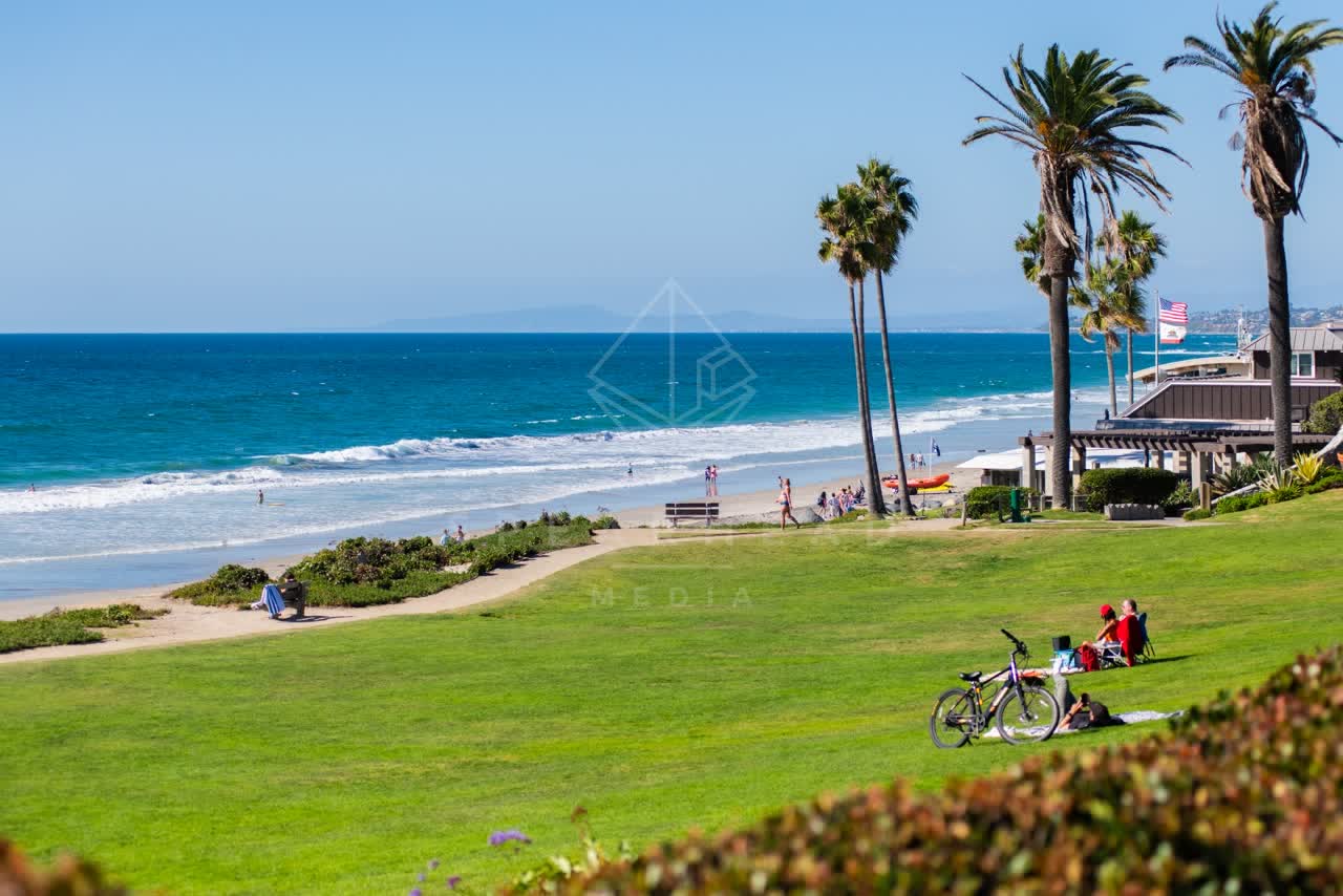 Elevated view of the beach, the surf and palm trees at Powerhouse Park, with a crowd gathered.