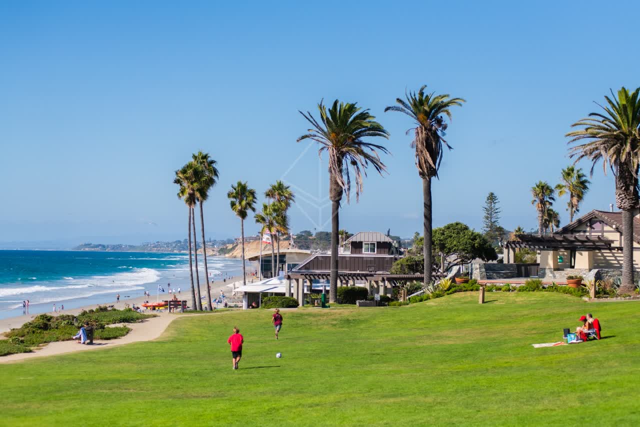 Elevated view of a park, the surf and palm trees at Powerhouse Park, with people walking.