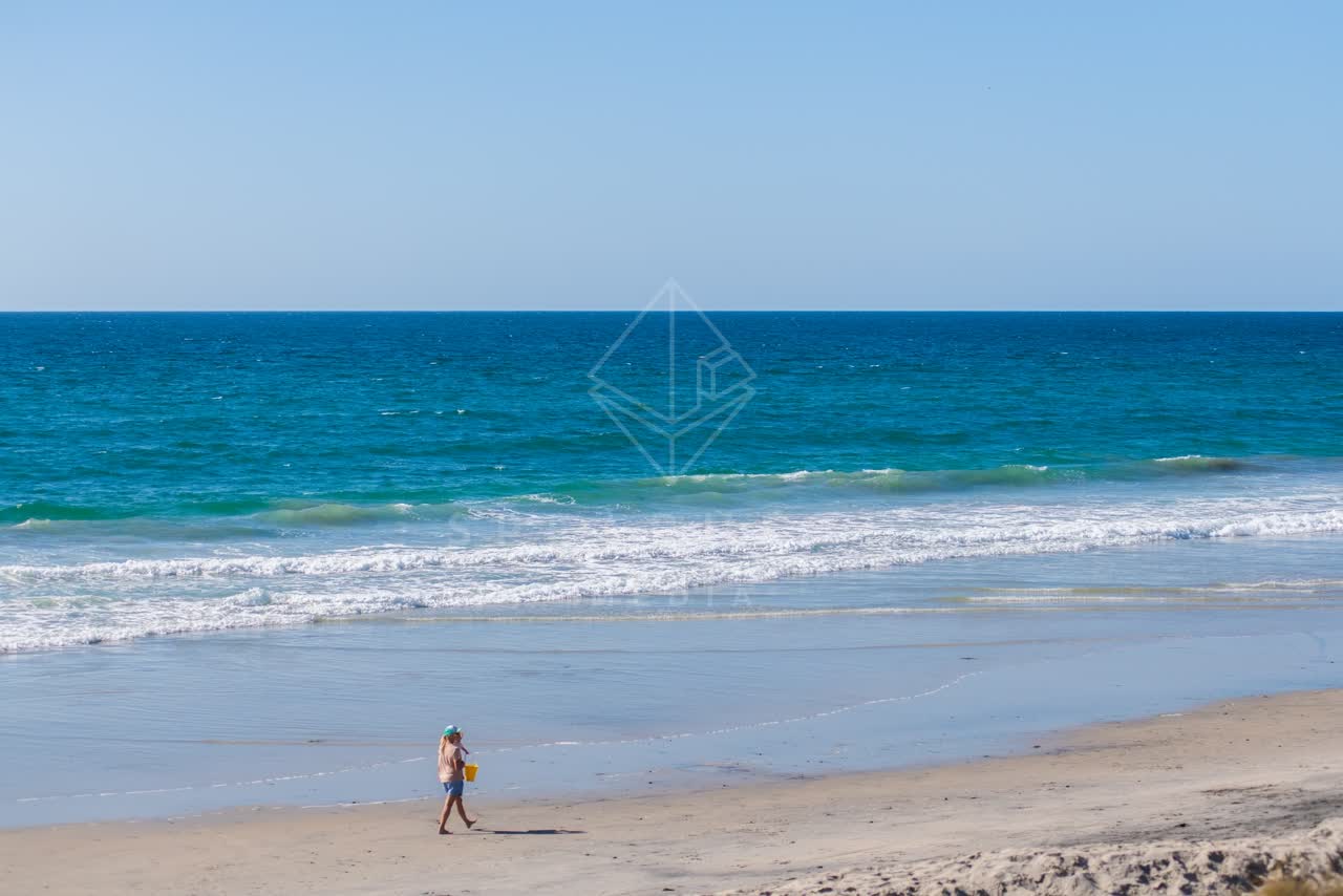 The beach, the surf and the ocean at Powerhouse Park, with people walking.