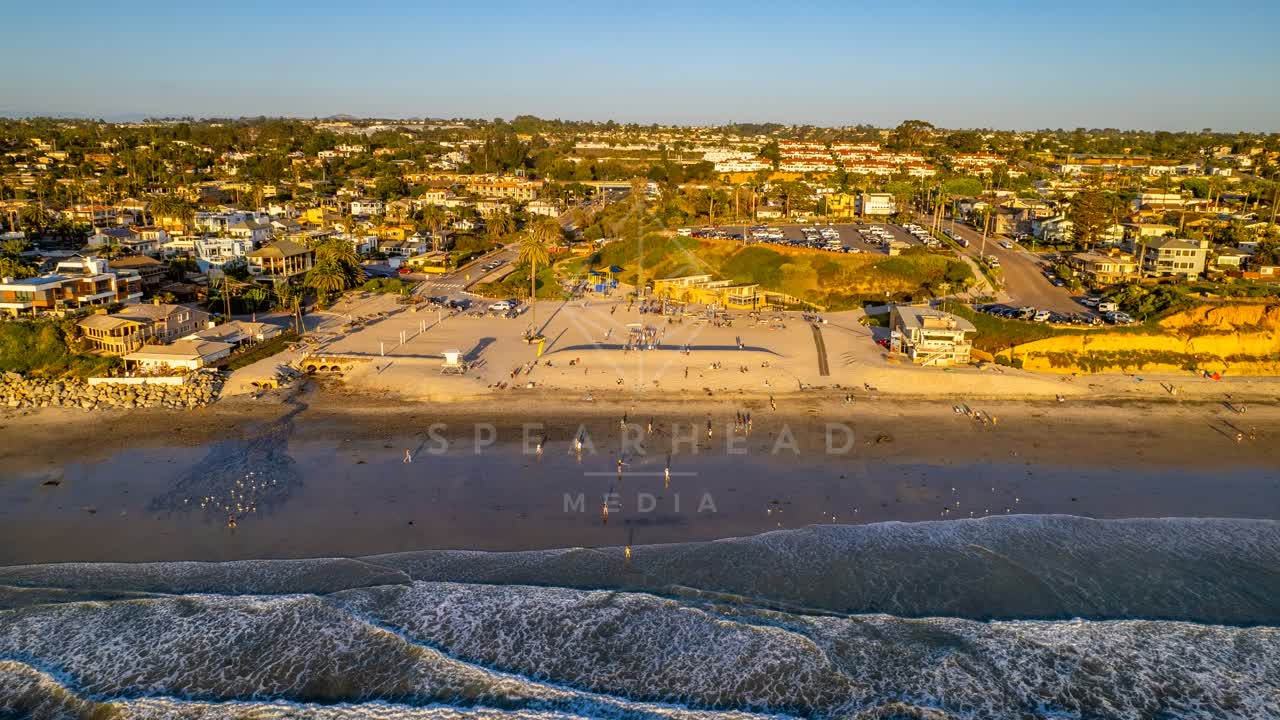 Aerial view of the beach, the surf and palm trees at Moonlight Beach, with people walking.