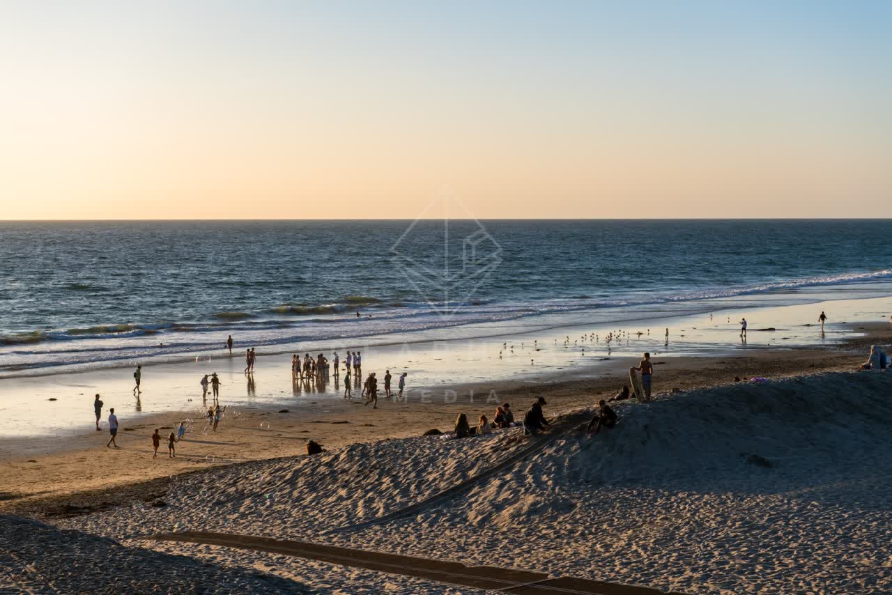 Elevated view of the beach, the surf and the ocean at Moonlight Beach, with a crowd gathered.