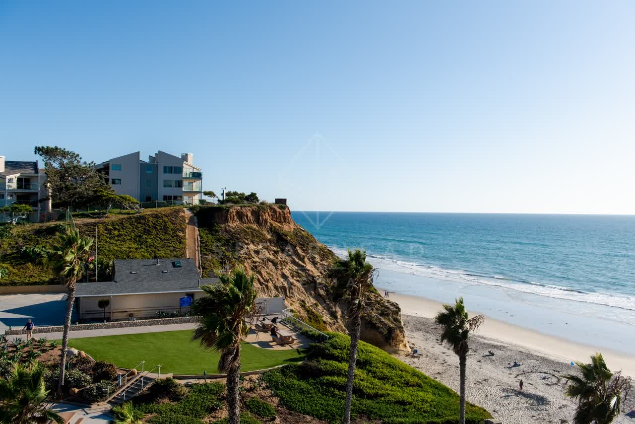 Low aerial view of the beach, palm trees and the ocean at Fletcher Cove, with people walking.