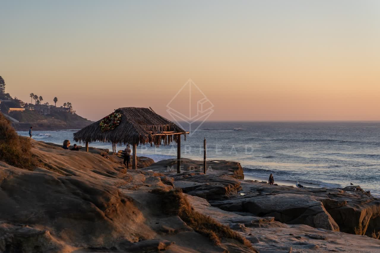 Elevated view of the cliffs, the surf and palm trees at Windansea, with people walking.