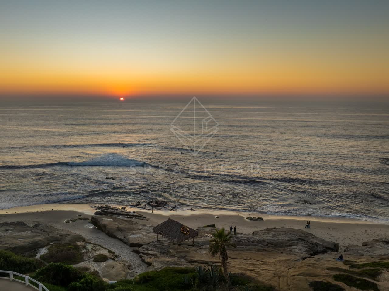 Aerial view of the cliffs, the surf and palm trees at Windansea, with surfers out.