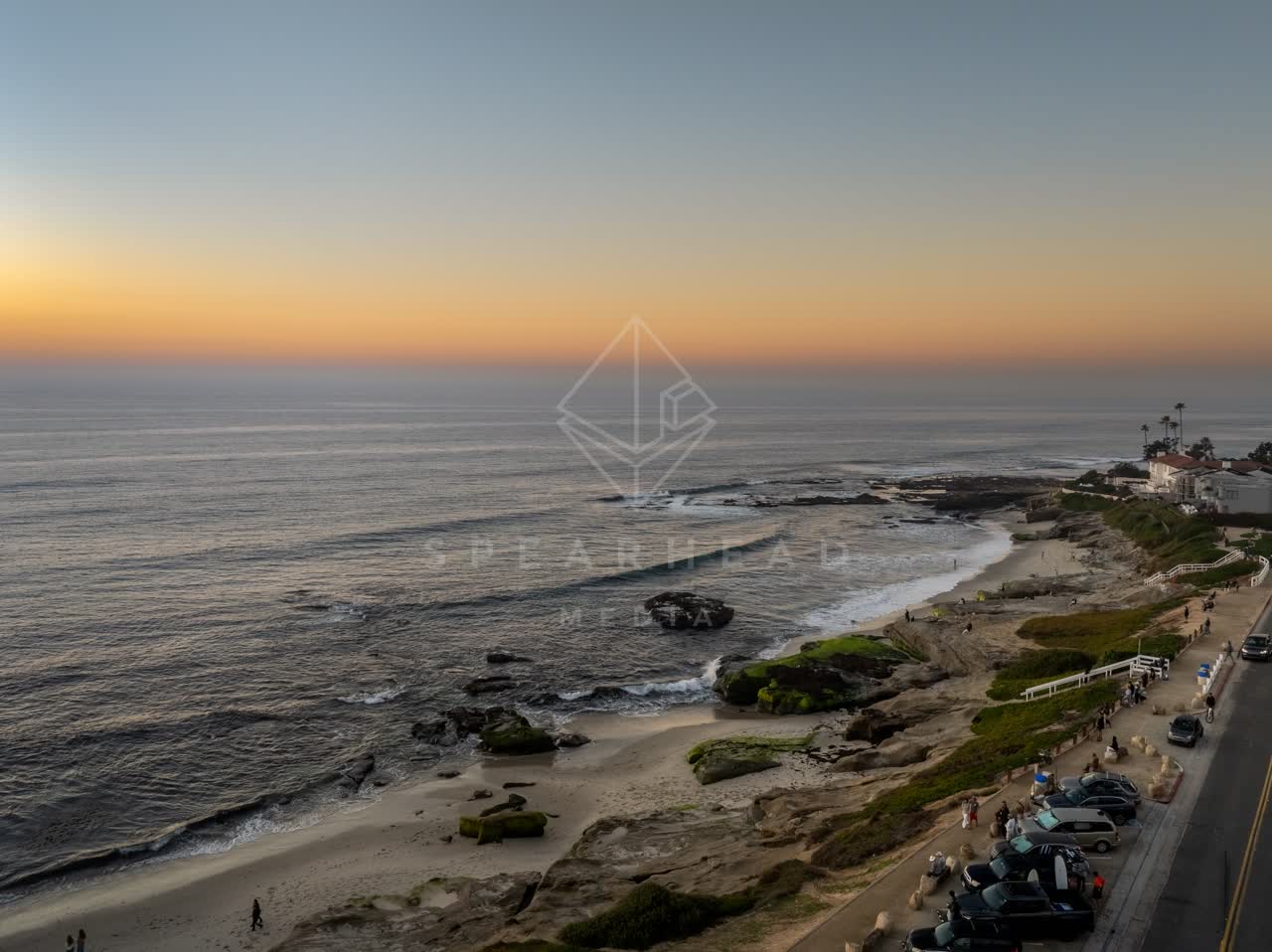 Aerial view of the cliffs, the ocean and homes at Windansea, with people walking.
