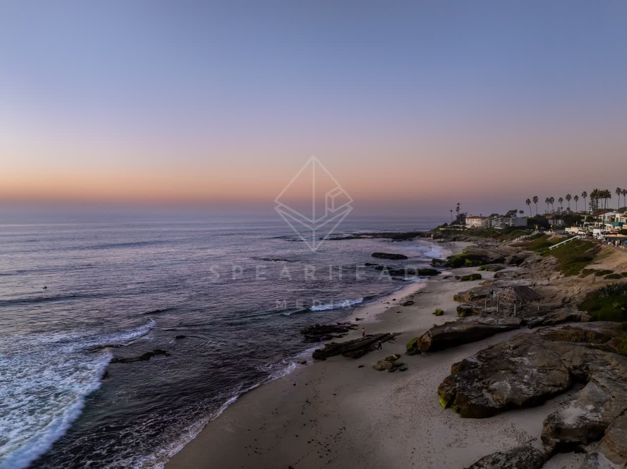 Low aerial view of the cliffs, the surf and palm trees at Windansea, with people walking.