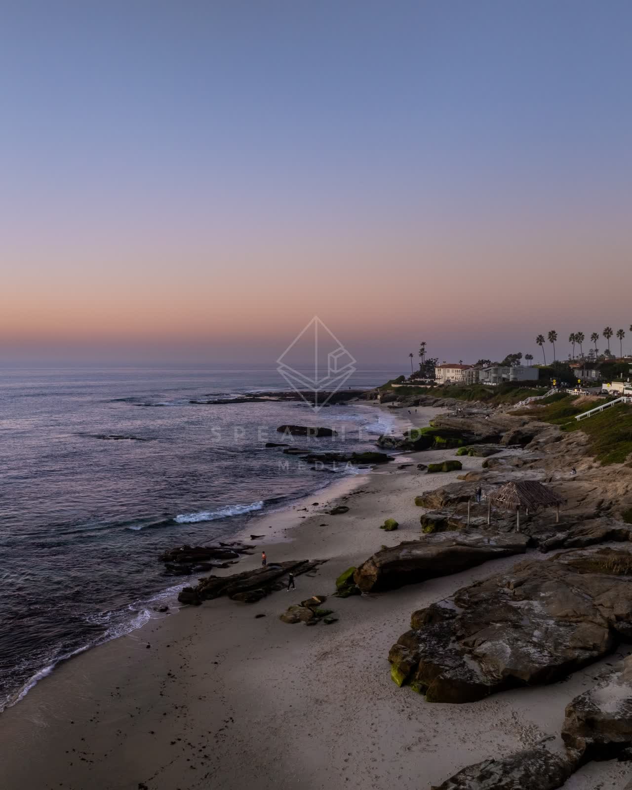 Low aerial view of the beach, palm trees and the ocean at Windansea, with people walking.