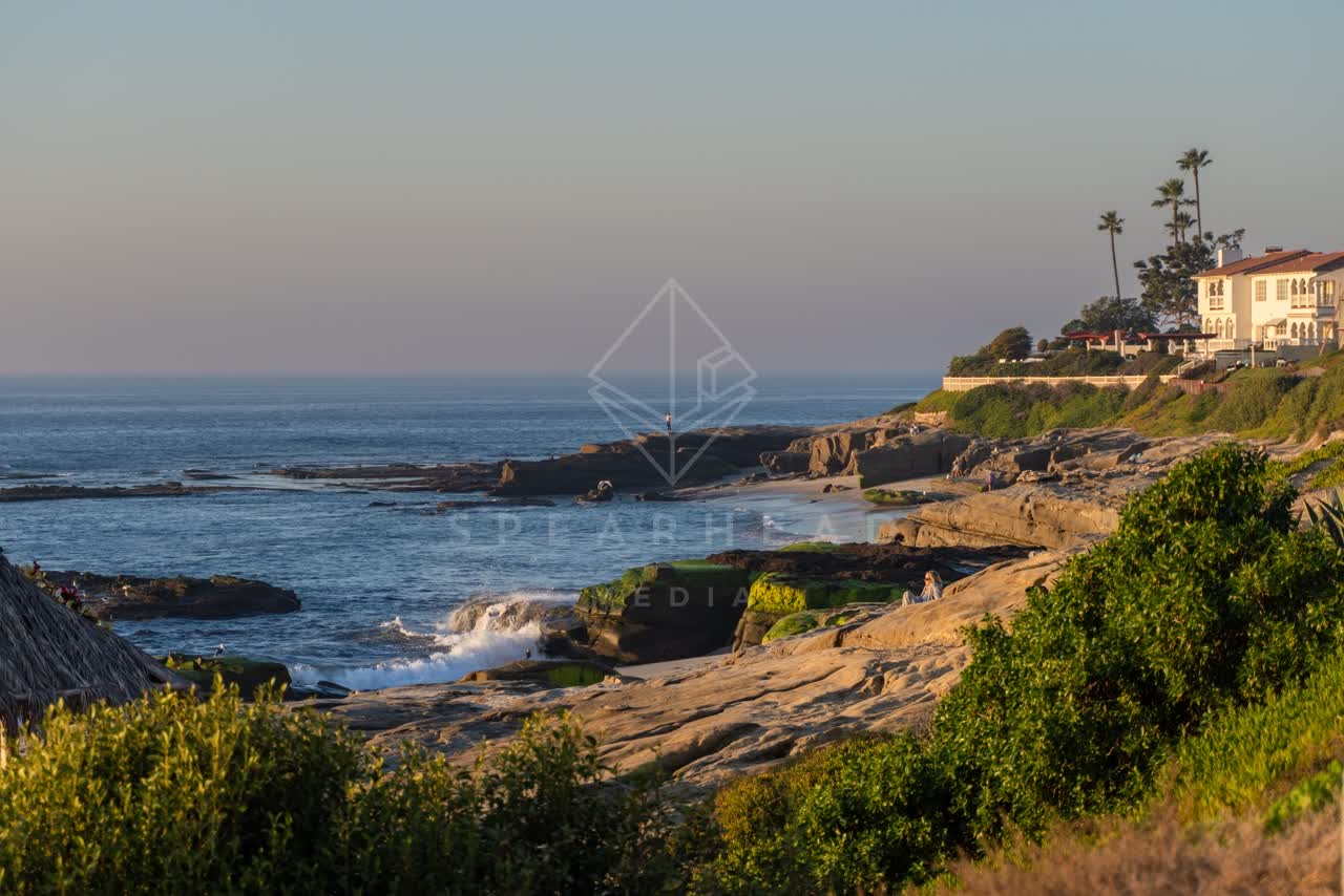 Elevated view of the cliffs, the surf and palm trees at Windansea, with people walking.