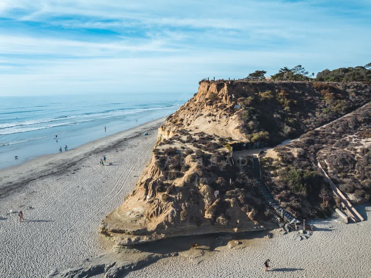 Aerial view of the cliffs, the ocean and the beach at Del Mar Dog Beach, with people walking.