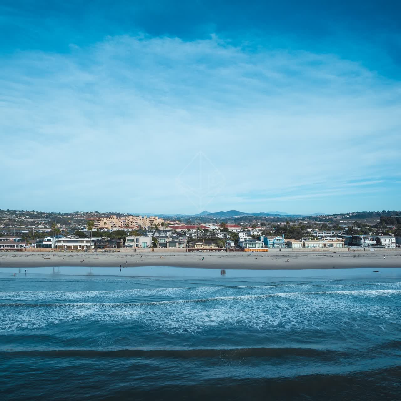 The beach, the surf and the ocean at Del Mar Dog Beach, with people walking.