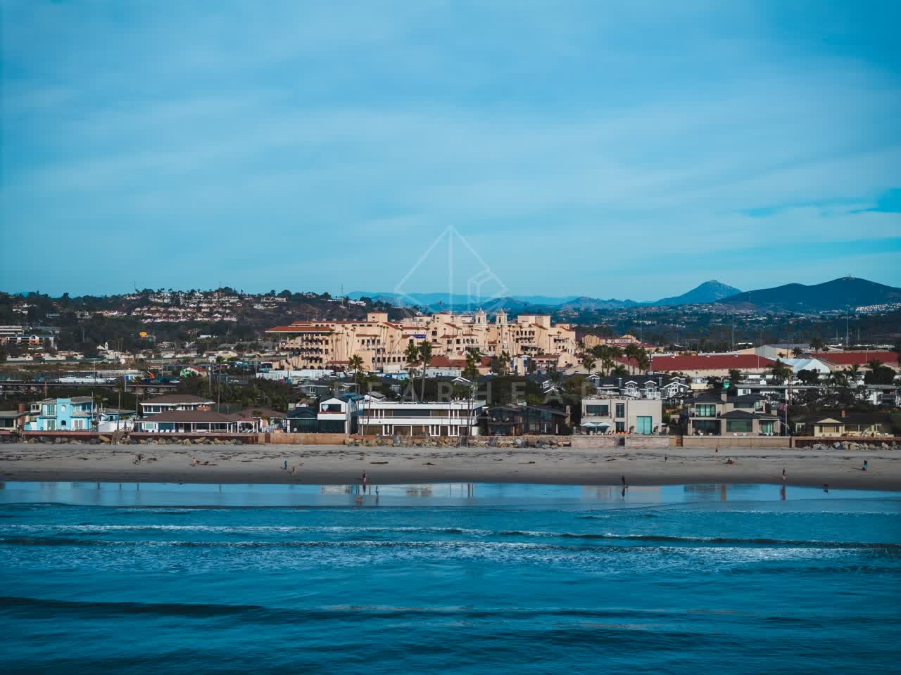 The beach, palm trees and the ocean at Del Mar Dog Beach, with people walking.