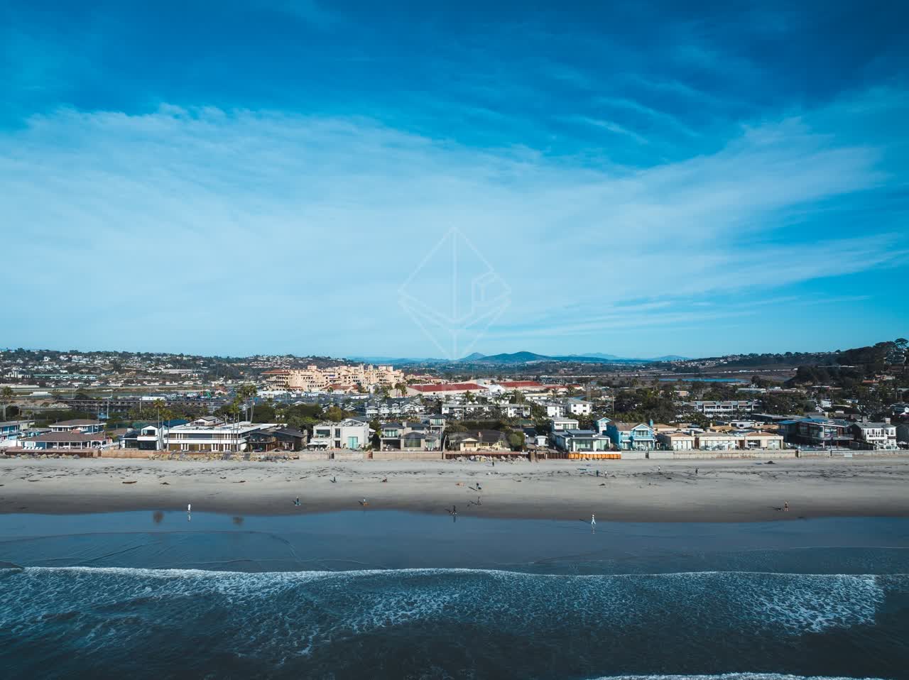 Low aerial view of the beach, the surf and the ocean at Del Mar Dog Beach, with people walking.