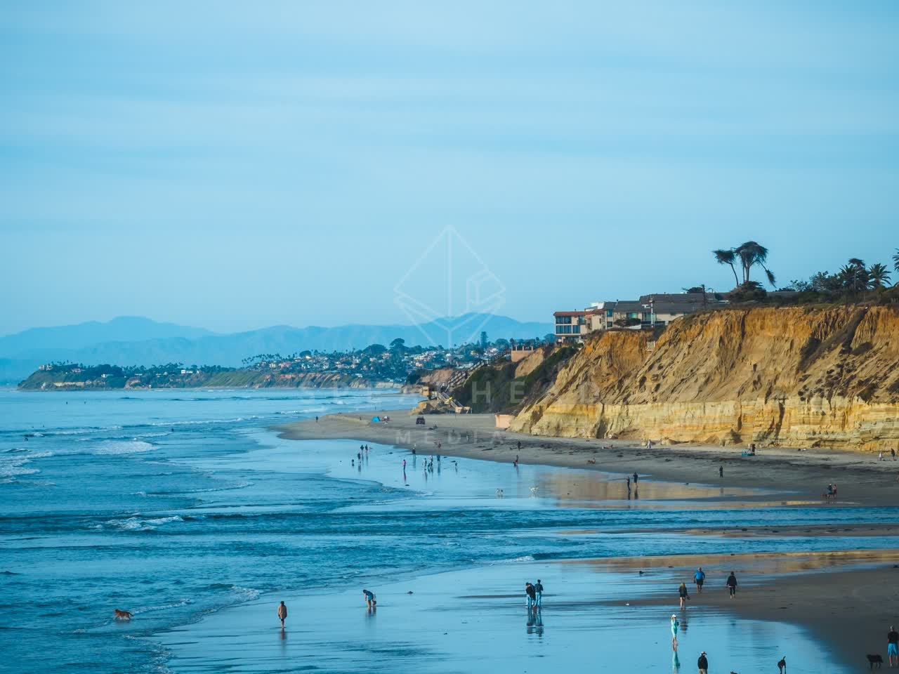 Low aerial view of the beach, wildlife and the ocean at Del Mar Dog Beach, with people walking.