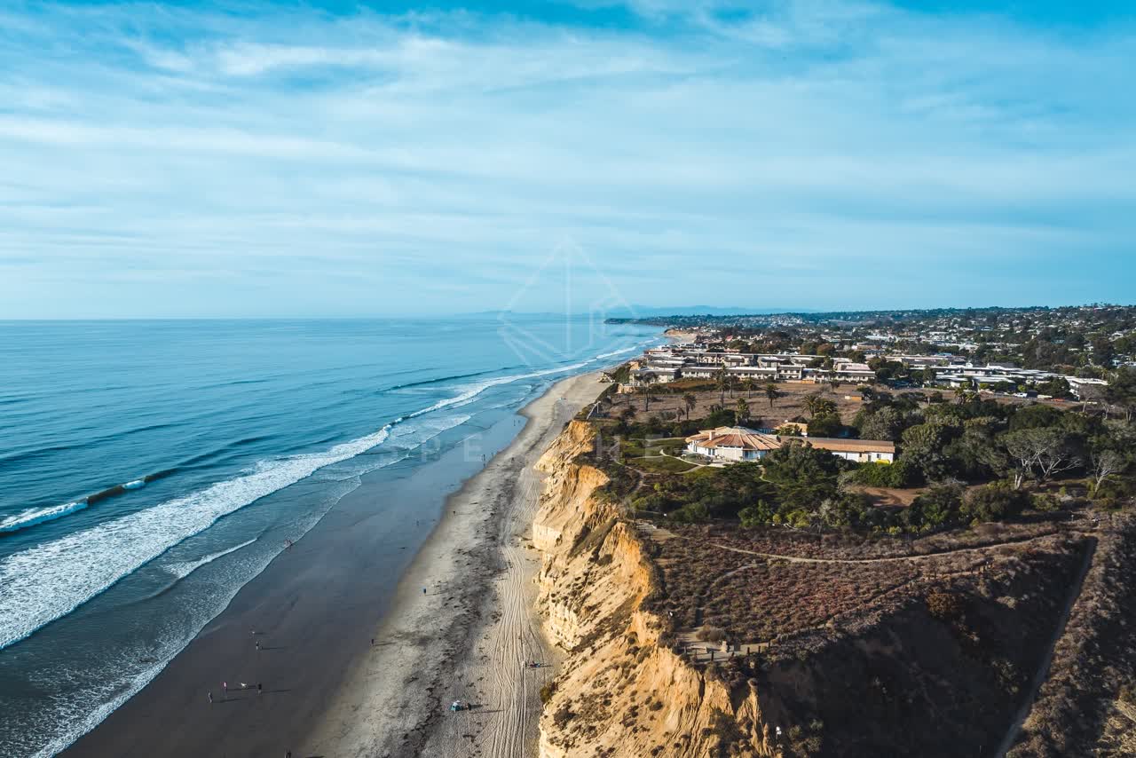 Aerial view of the cliffs, the ocean and homes at Del Mar Dog Beach, with people walking.