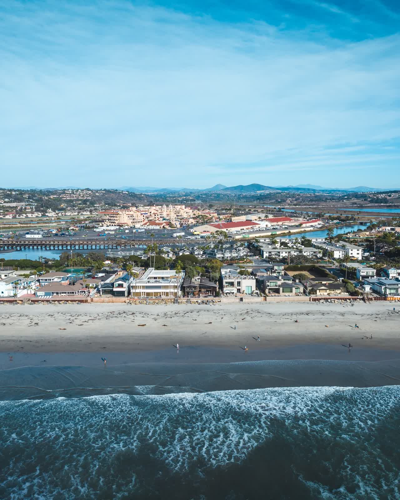 Aerial view of the beach, the surf and the bridge at Del Mar Dog Beach, with people walking.
