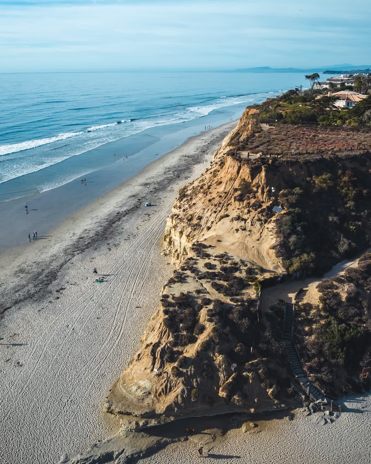 Aerial view of the cliffs, the surf and the ocean at Del Mar Dog Beach, with people walking.