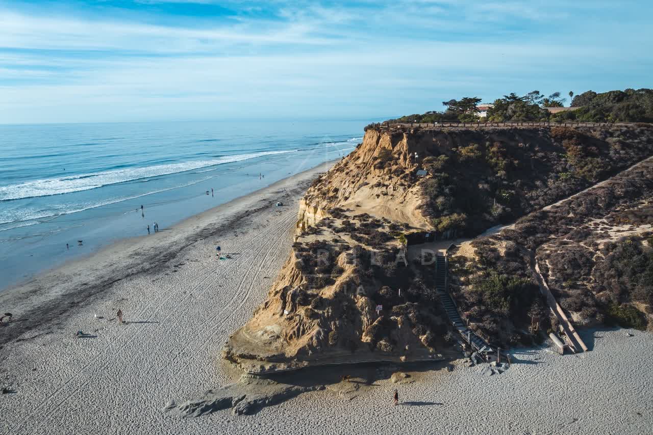 Aerial view of the cliffs, the surf and the ocean at Del Mar Dog Beach, with people walking.