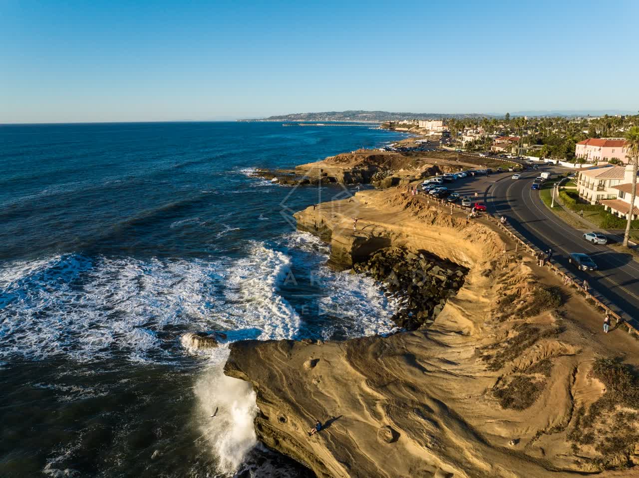Aerial view of the cliffs, the surf and palm trees at Sunset Cliffs, with people walking.