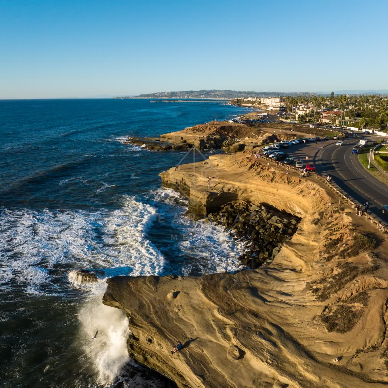 Aerial view of the cliffs, the surf and the pier at Sunset Cliffs, with people walking.
