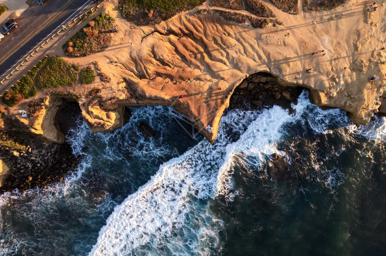 Aerial view of the cliffs, the surf and the ocean at Sunset Cliffs, with people walking.